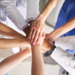 A team of healthcare professionals putting their hands on top of each other in a circle