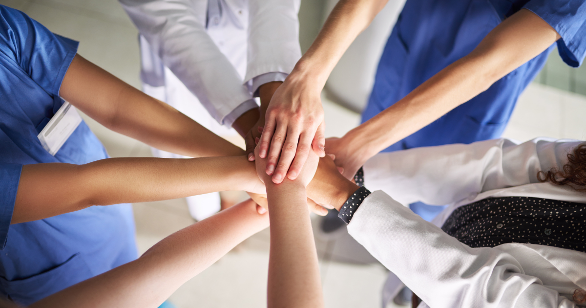 A team of healthcare professionals putting their hands on top of each other in a circle
